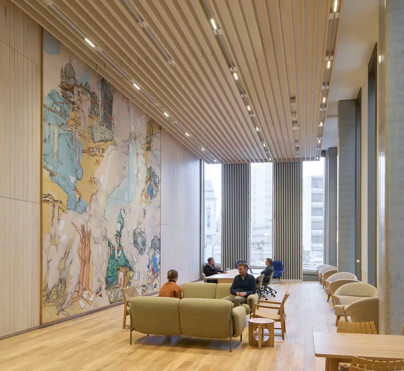 Lounge space with large tapestry wall hanging and green seating under diagonal wood slat ceiling