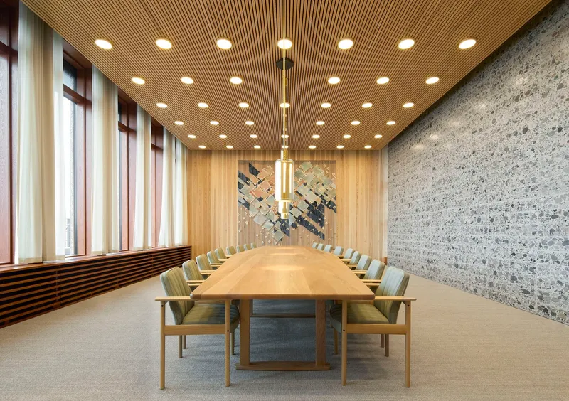 Conference room with long timber table beneath recessed circular ceiling lights and exposed aggregate wall