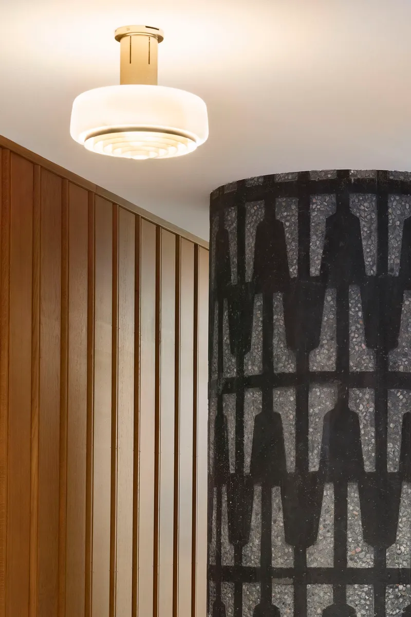Flush-mounted white glass pendant light with brass fitting above vertical wood paneling and patterned dark wallcovering