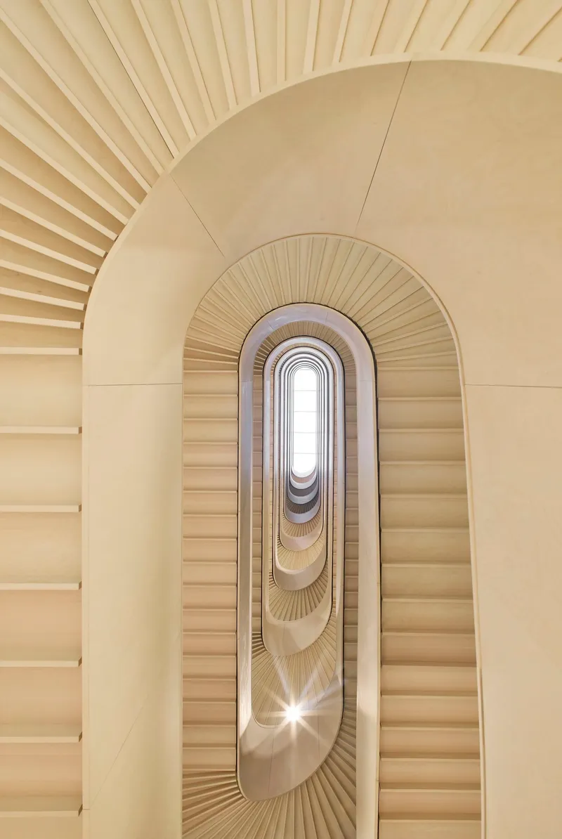 Upward view through oval stairwell with radiating handrails and skylight at summit creating bright central glow