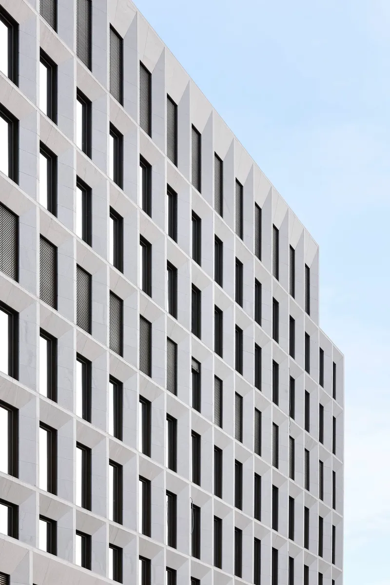 White precast concrete facade with rhythmic pattern of deep-set rectangular window openings under overcast sky