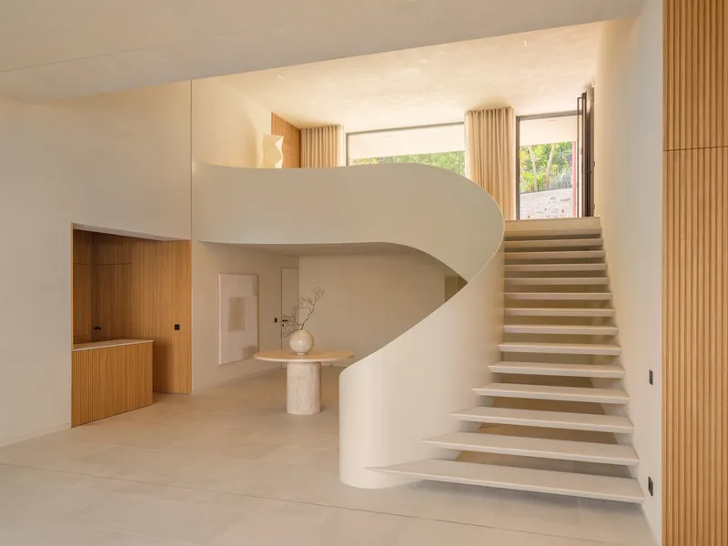 Helical staircase with pale stone treads rising toward a window framed by timber slat columns