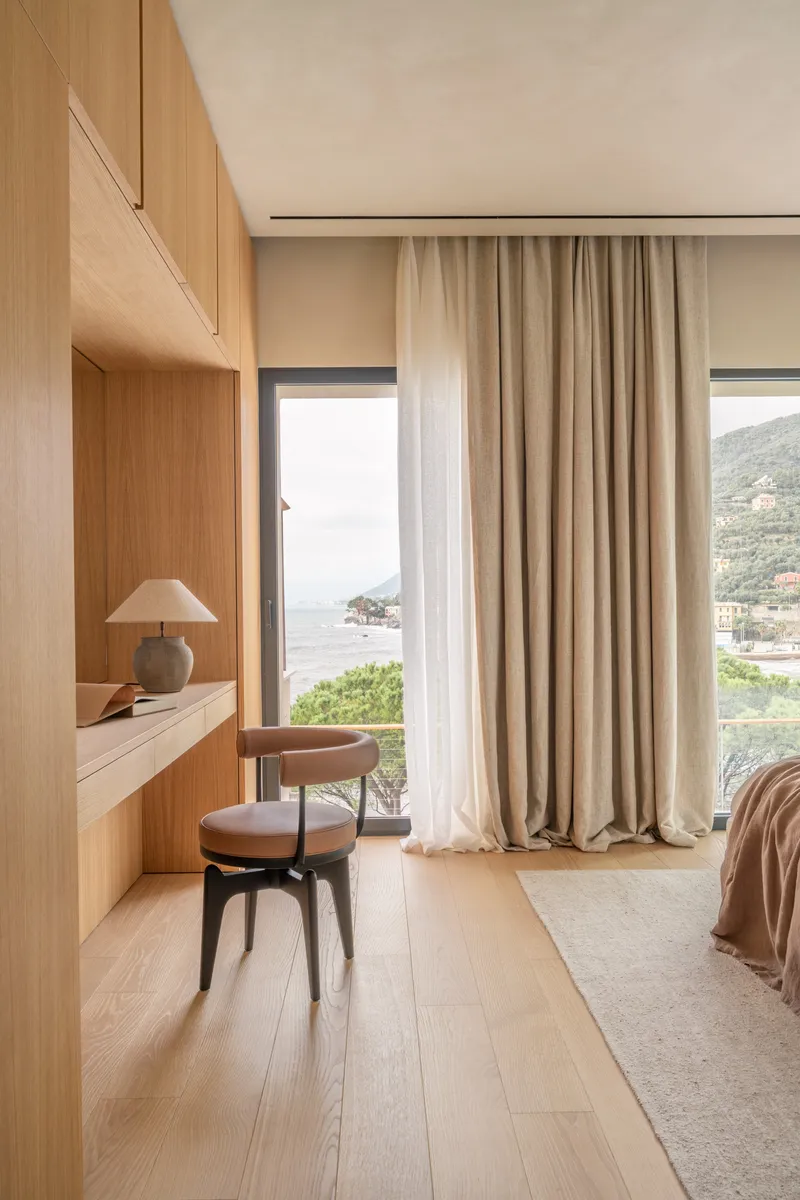 Built-in oak desk and chair beside a window overlooking coastal hills in afternoon light