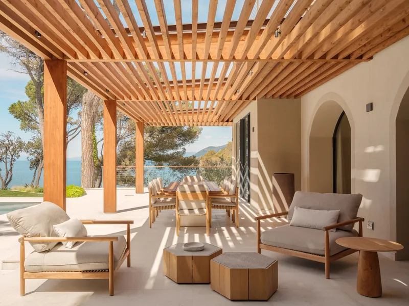 Covered terrace with timber pergola casting striped shadows across lounge furniture and stone pavers