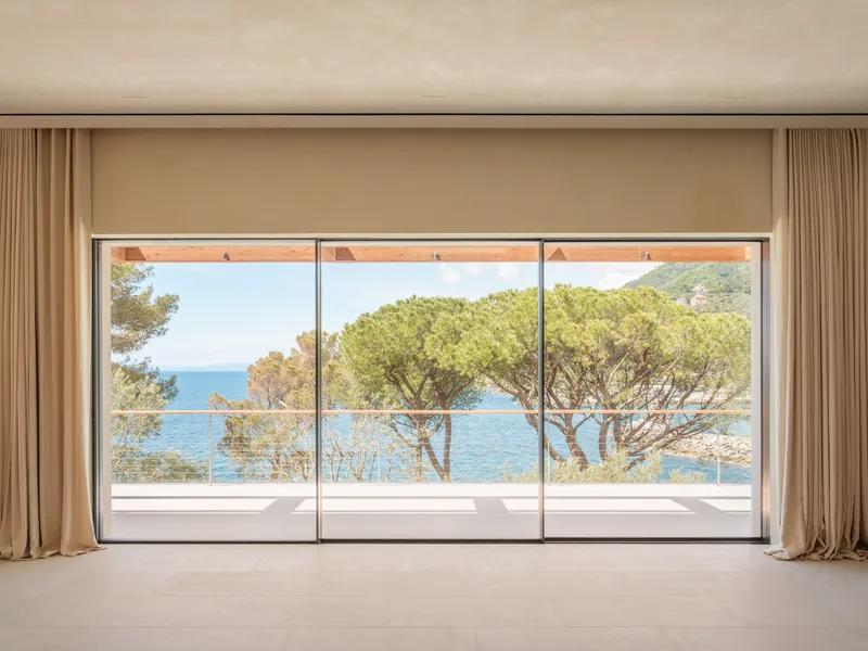 Floor-to-ceiling glazed doors framing pine trees and coastal view beyond a glass balustrade