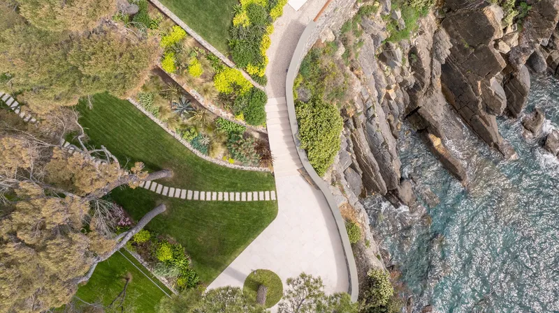 Aerial view of curved stone staircase descending terraced gardens toward the rocky coastline