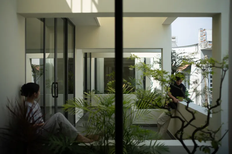Interior courtyard glimpsed through glass doors with two residents and planted palms in filtered light