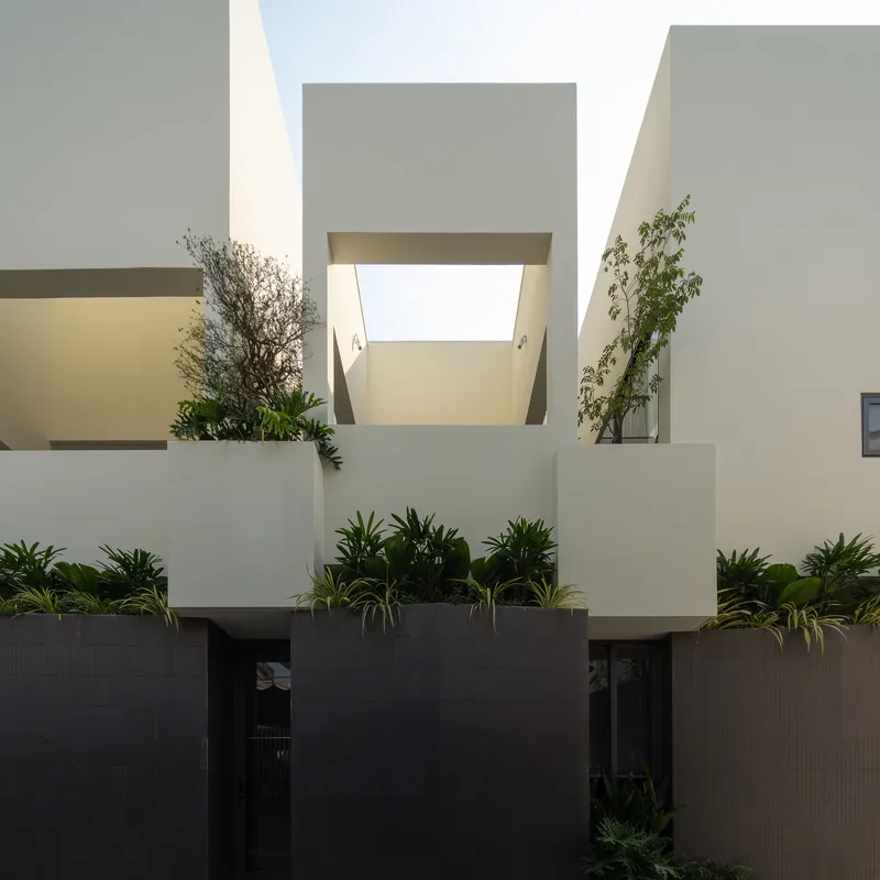 Street view of stacked white volumes with planted terraces above a dark tiled base at dusk