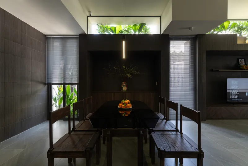 Dining area with timber table and benches beneath a high clerestory window filled with palm fronds