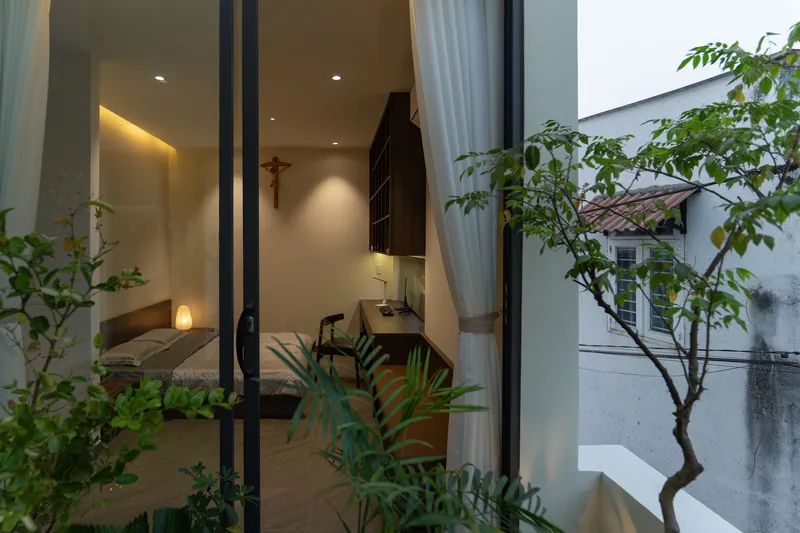 Bedroom viewed through open glass doors from the planted courtyard at dusk with interior lights glowing
