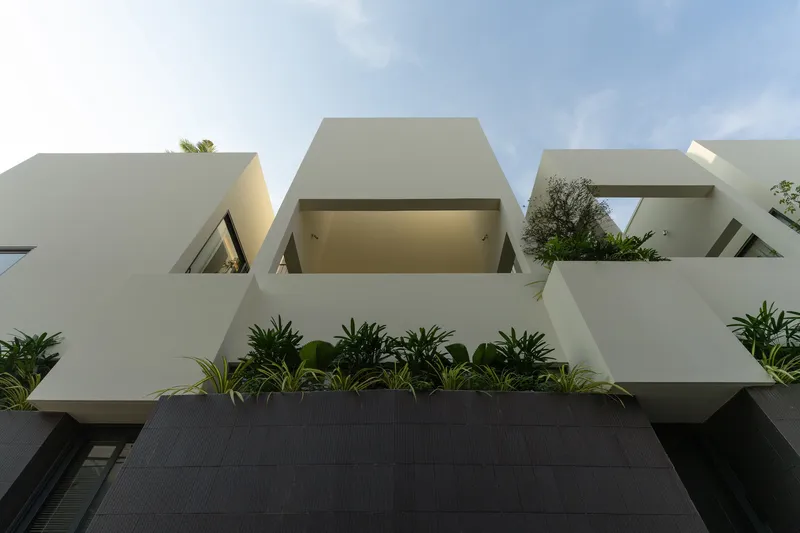 Upward view of the cantilevered white volumes with planted terraces against a cloudy sky