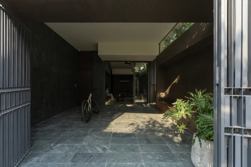 Covered entry courtyard with dark stone paving, vertical metal screening, and potted ferns in afternoon sunlight