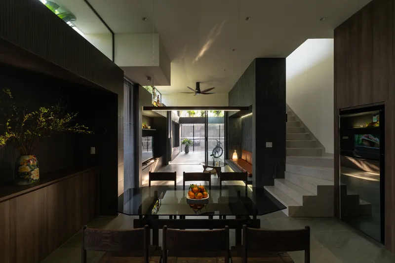 Double-height dining area with dark timber joinery, floating staircase, and view through to rear courtyard