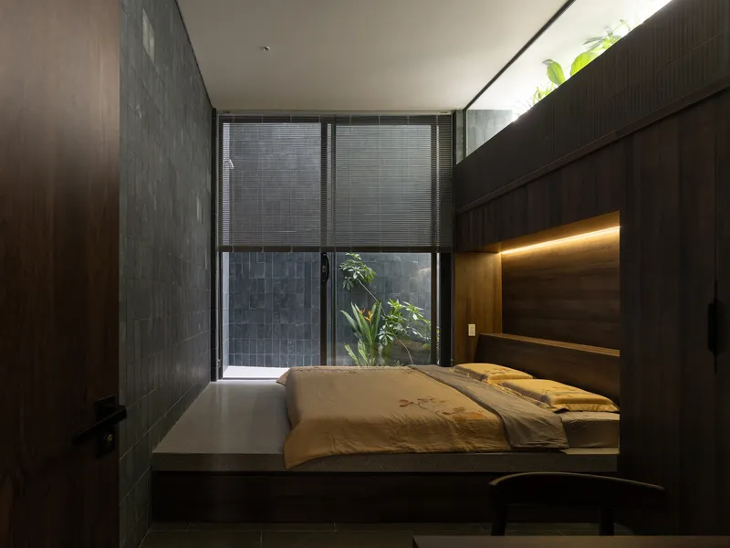 Bedroom with platform bed against timber wall, translucent sliding screen, and planted lightwell beyond