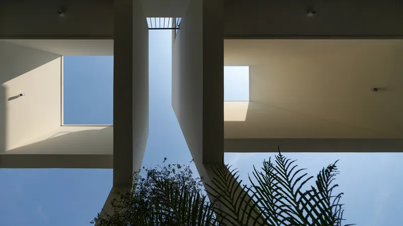 Looking up at interior courtyard with concrete beam, skylight above, and palm fronds at base