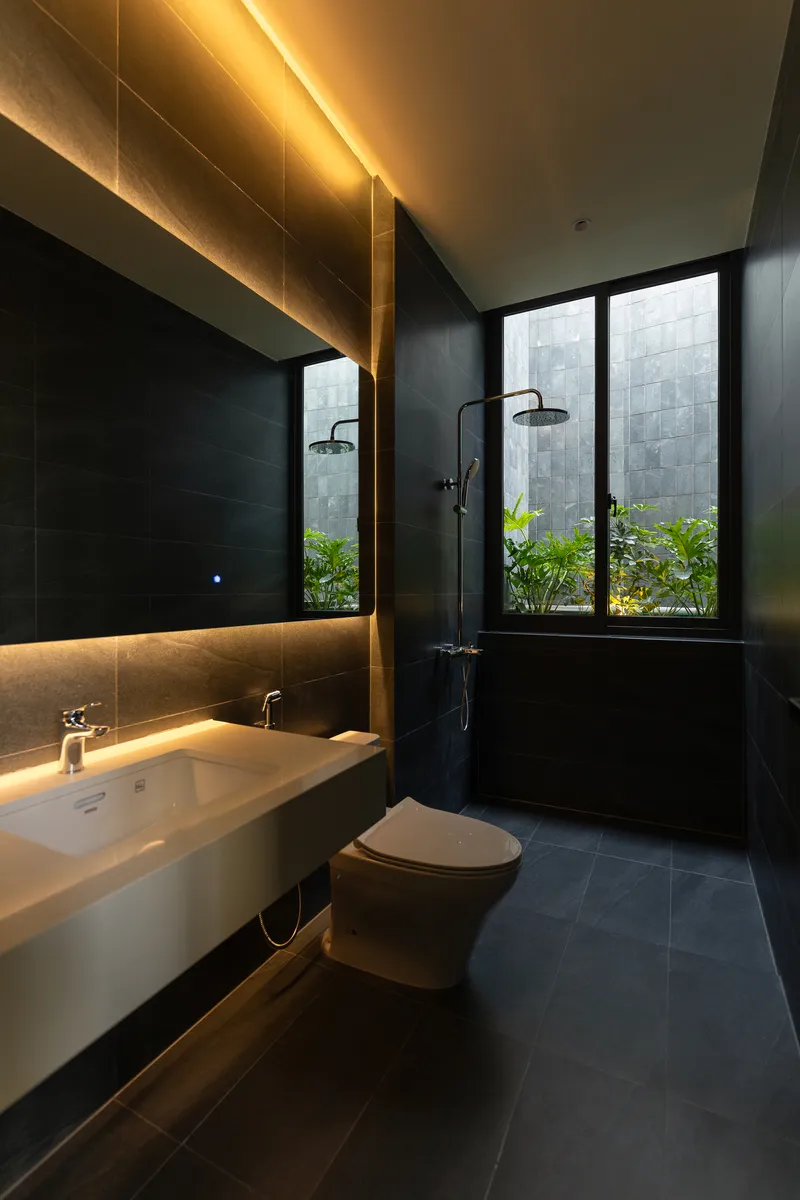Bathroom with backlit mirror, floating vanity, and window overlooking a planted courtyard with grey tile walls