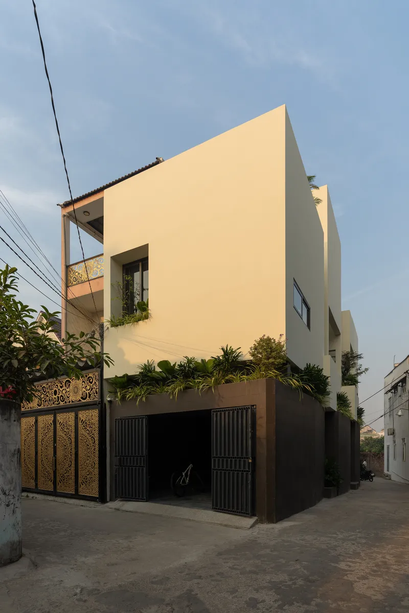 Street corner view of the pale stucco facade with perforated metal garage doors and rooftop planting
