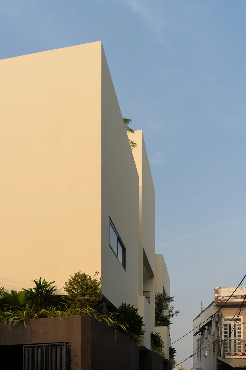 Corner view of the pale stucco facade with angular volumes and lush plantings at the base