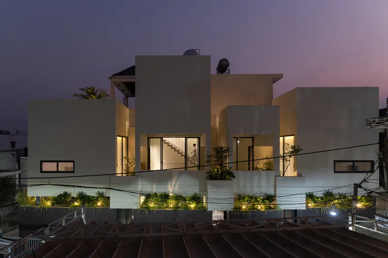 Street facade with stacked white volumes and illuminated planted terraces at dusk