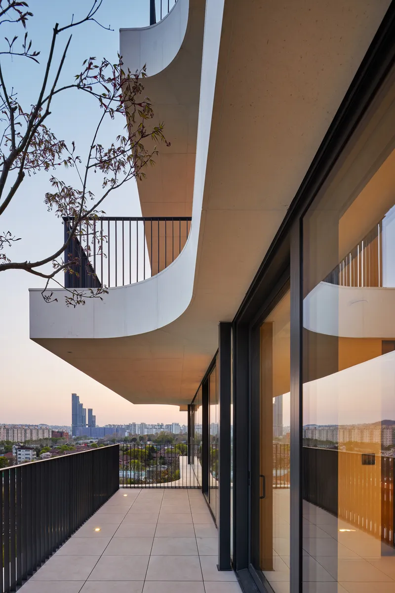 Cantilevered balconies with curved soffit edges and a bare tree branch at dusk