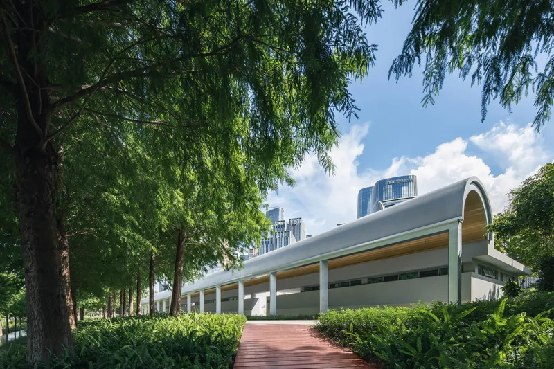 Barrel-vaulted roof above a colonnade entry plaza framed by willow trees and trimmed hedges