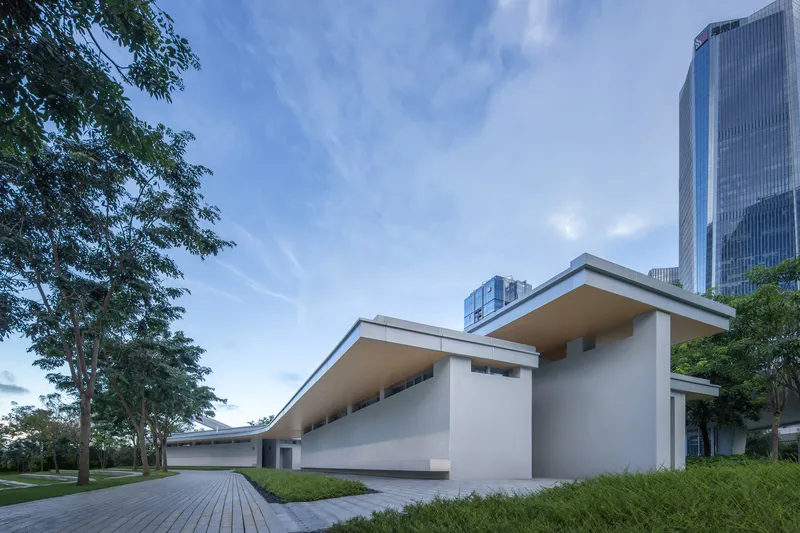 Asymmetrical paired vaulted roofs rising over white stucco walls at dusk with highrise towers beyond