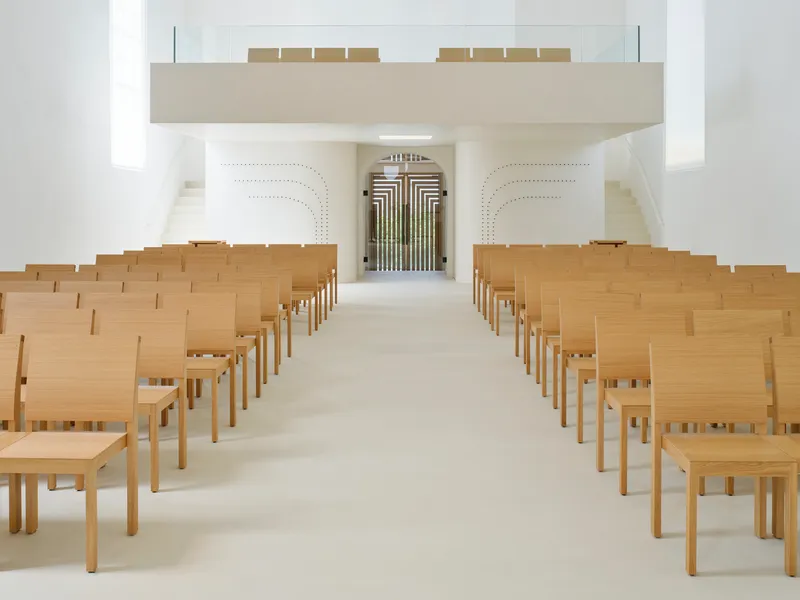 Rows of oak seating under cantilevered gallery facing perforated choir screen and organ pipes