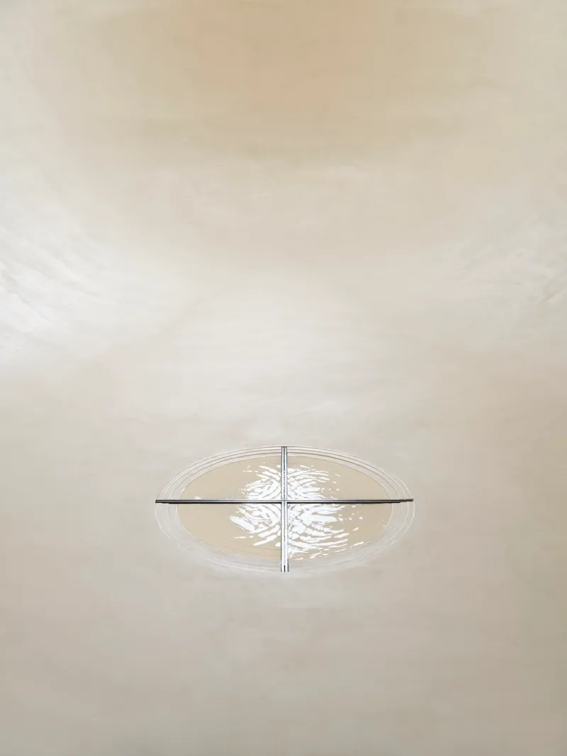 Overhead view of cruciform light fixture casting patterned shadows on curved white plaster vault