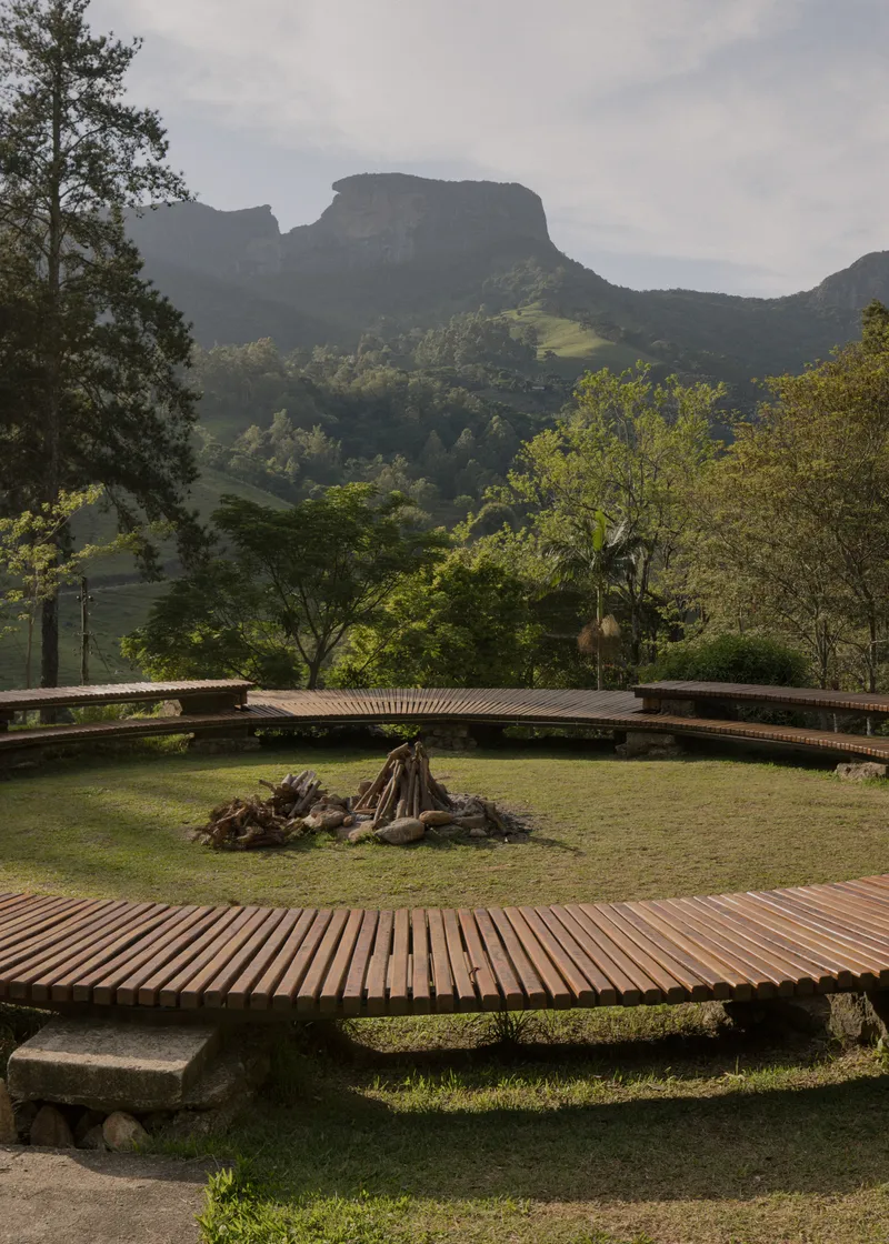 Circular timber deck platforms on grass with a central fire pit overlooking forested mountains
