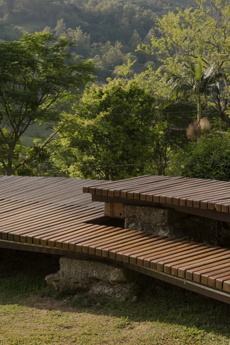 Close-up of slatted timber deck benches supported by rough stone bases in dappled sunlight