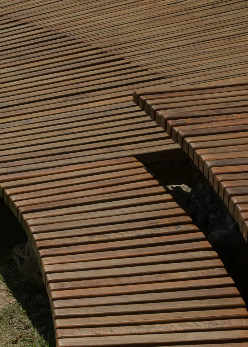 Overhead view of intersecting timber slatted decks casting diagonal shadows on the ground