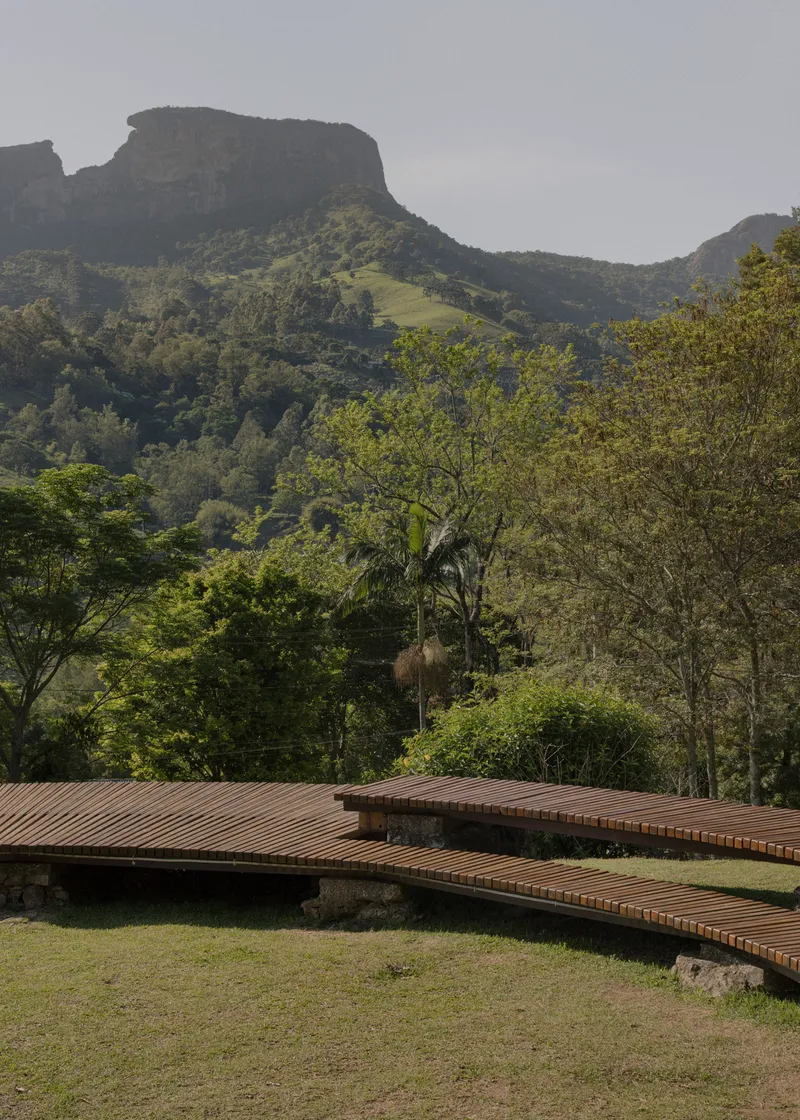 Slatted timber walkway extending across lawn beneath forested mountain ridge
