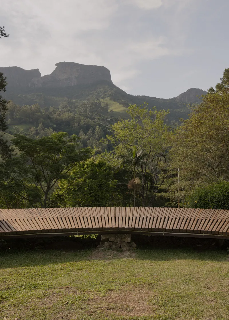 Horizontal slatted timber bridge spanning grass with mountain cliffs rising behind in mist