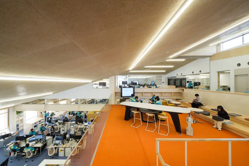 Two-story office interior with orange floor graphics, tiered seating, and employees working at desks below