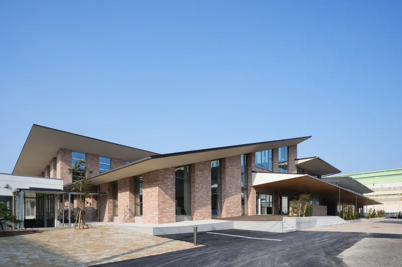 Entrance facade with layered cantilevered roofs, brick volumes, and planted beds in afternoon light