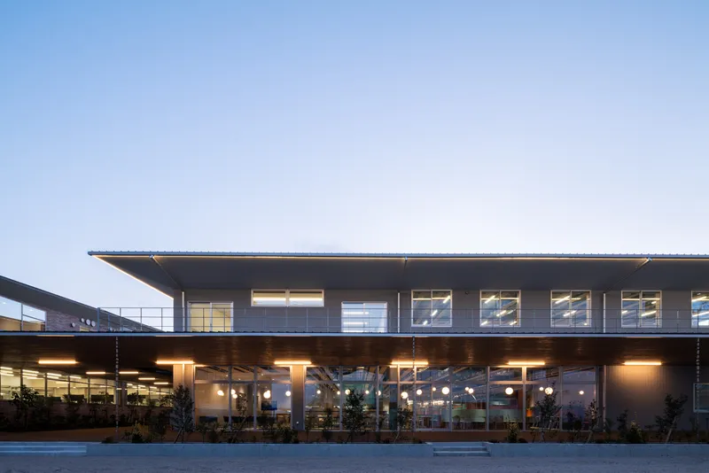 Cantilevered upper floor and recessed ground-level colonnade with globe pendant lights at twilight