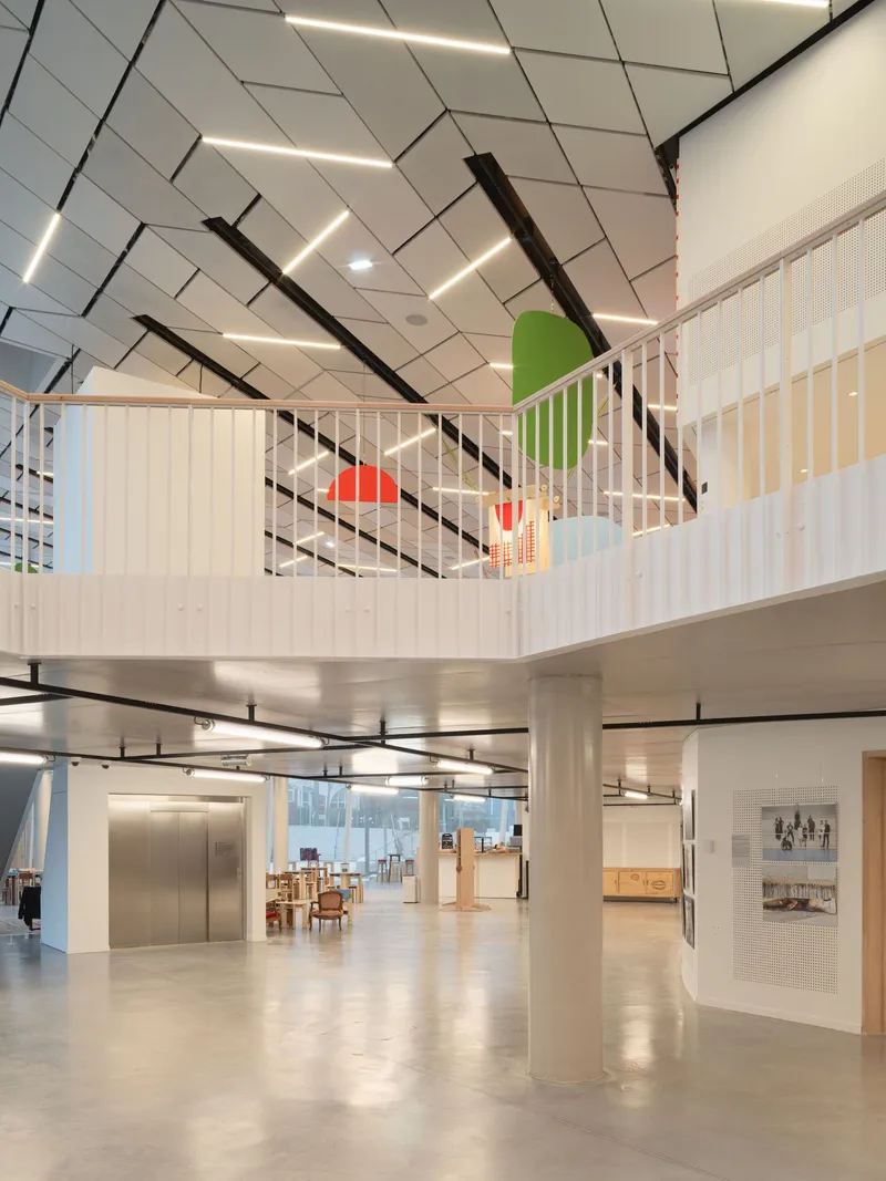 Interior atrium looking up to mezzanine with vertical slat railings and angular white ceiling panels
