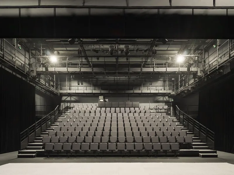 Frontal view of the theatre auditorium with tiered seating and exposed lighting rigging overhead