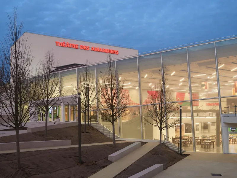 Entrance approach at twilight with bare winter trees and illuminated double-height interior