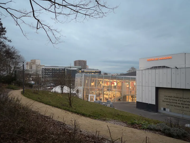 Illuminated glass facade with metal panel cladding viewed from a park path at dusk