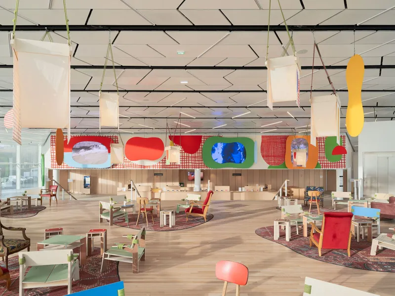 Open interior hall with suspended fabric panels, varied seating and colorful artworks on mezzanine