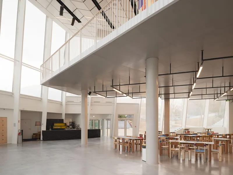 Double-height entry hall with white cylindrical columns, suspended mezzanine, and timber dining furniture