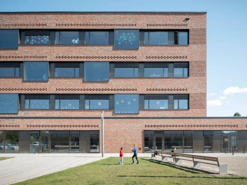 Brick facade with perforated horizontal bands and two figures walking on the lawn below