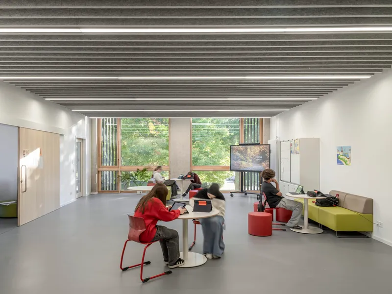 Classroom with slatted ceiling baffles, a window to greenery and students at low tables