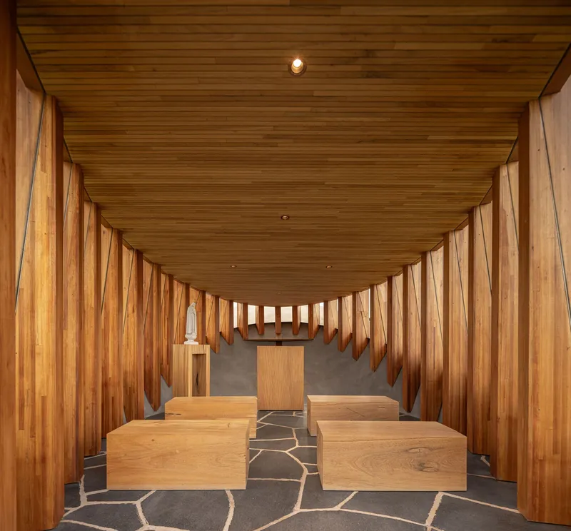 Interior chapel with vertical timber slat walls, curved timber ceiling and stone floor with timber benches