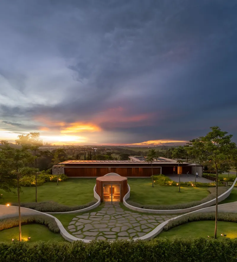 View across the entry forecourt showing symmetrical curving walls and the glowing pavilion at sunset