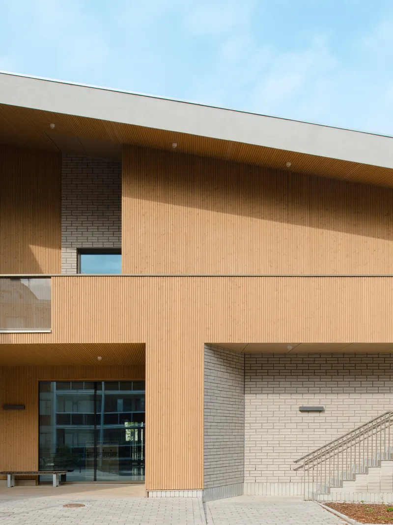 Entrance facade combining brick and timber slatted soffit with recessed balconies and exterior staircase