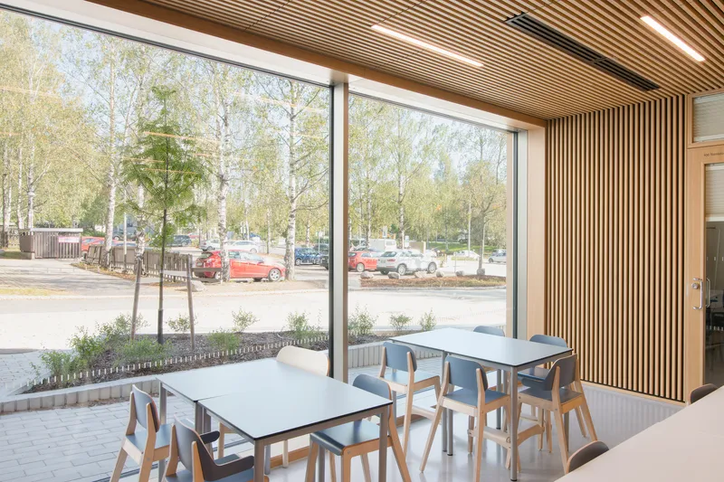 Dining area with timber slat wall, full-height glazing, and views of birch trees and parking