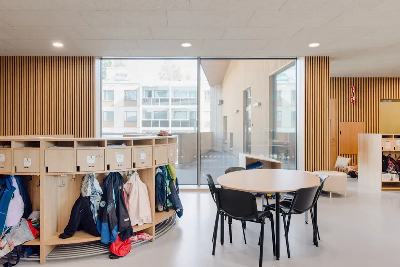 Classroom space with curved cubby storage, round table, and courtyard view through glazed partition