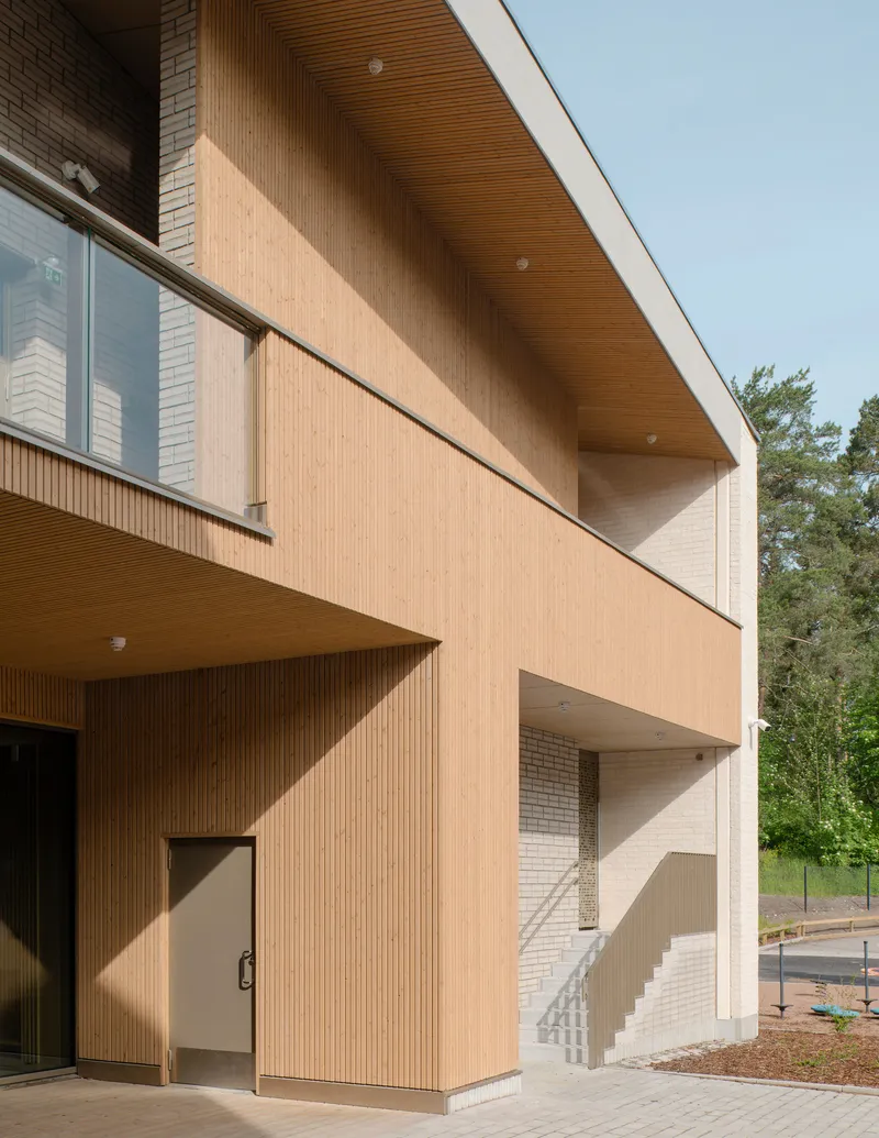 Timber-clad facade with recessed balconies and wood-slatted soffit under a clear sky